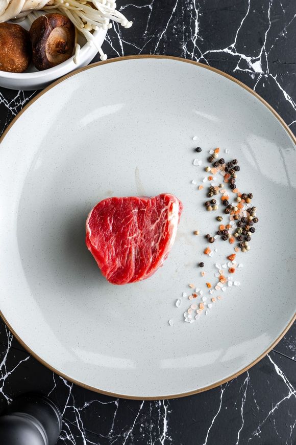 A piece of raw steak is on a black plate.