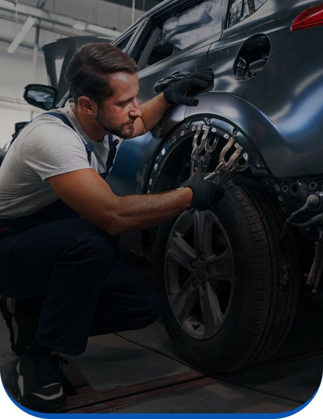 A man is working on the fender of a car in a garage.