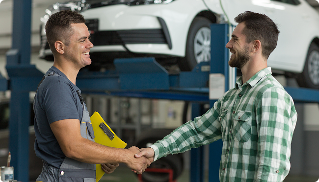 A man is shaking hands with a mechanic in a garage.