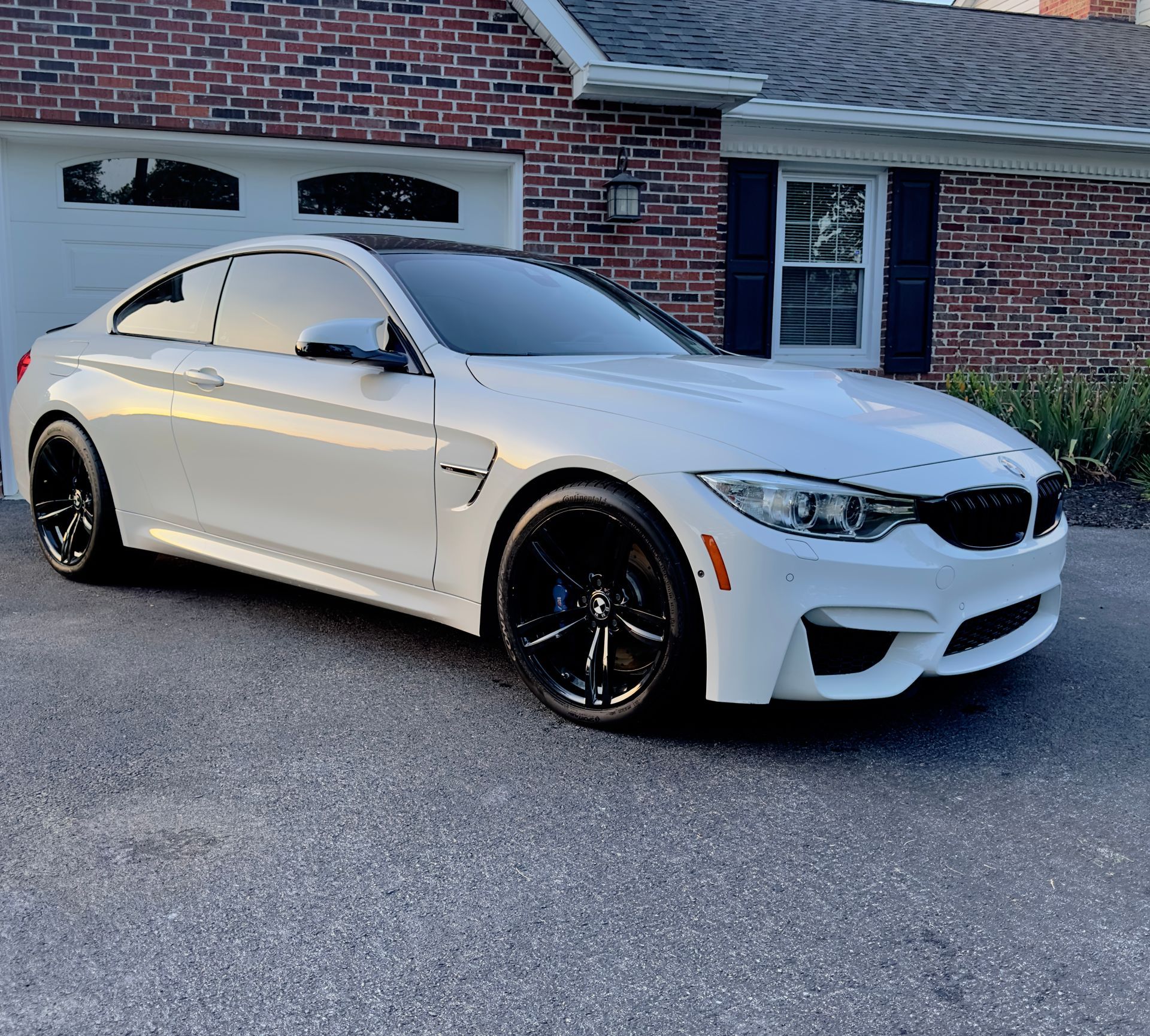 A white bmw is parked in front of a brick house