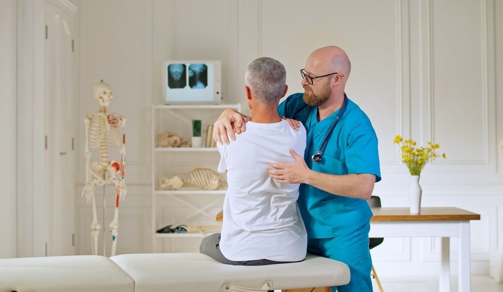 Doctor in Blue Scrubs Consulting With a Seated Patient — Back Care Gold Coast In Helensvale, QLD