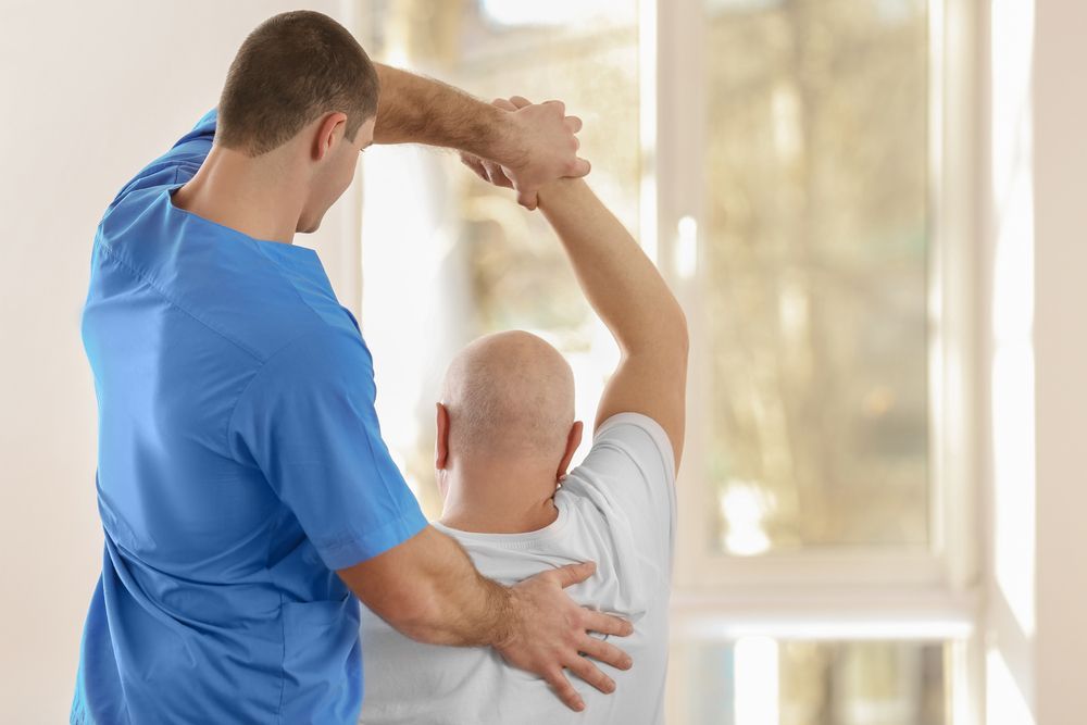 A Man is Helping Another Man Stretch His Arms — Back Care Gold Coast In Nerang, QLD