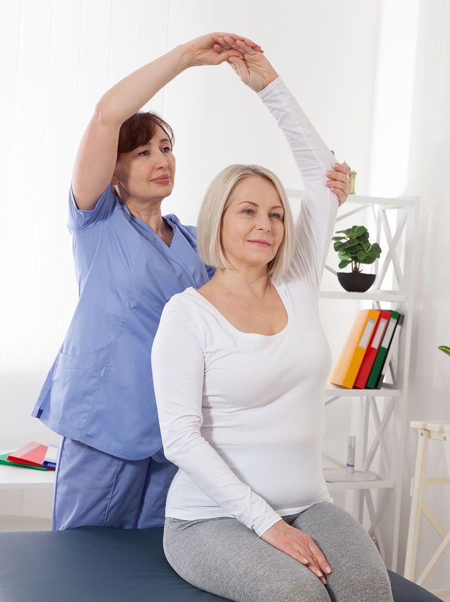 A Woman is Sitting on a Table While a Nurse Stretches Her Arm — Back Care Gold Coast In Nerang, QLD