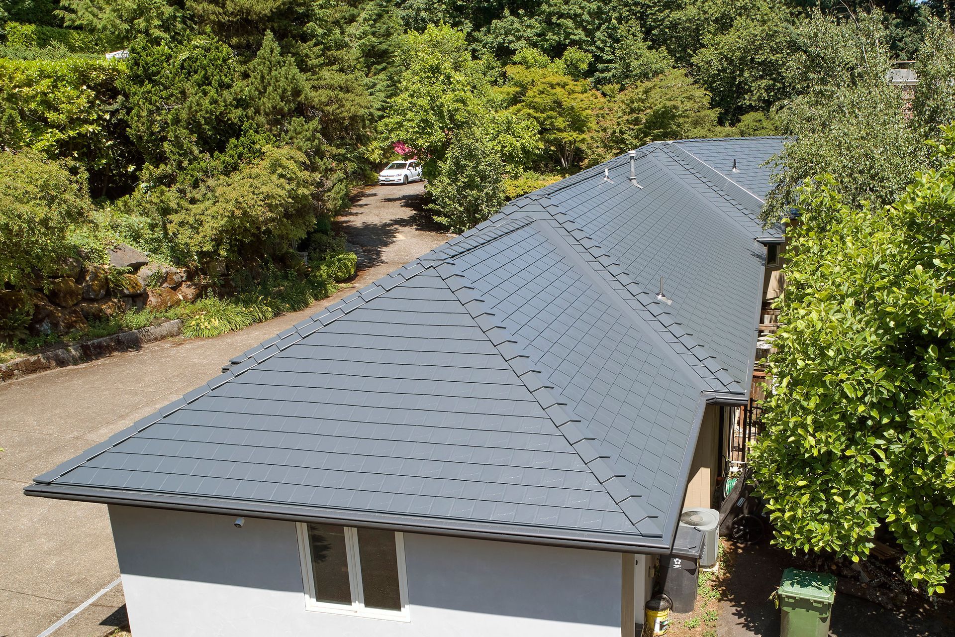 Side elevation of a Dunthorpe residence with a newly installed Deep Charcoal Interlock Slate roof made from heavy-gauge aluminum. The metal roof’s slate texture and color complement the estate’s light stucco siding and manicured landscaping.