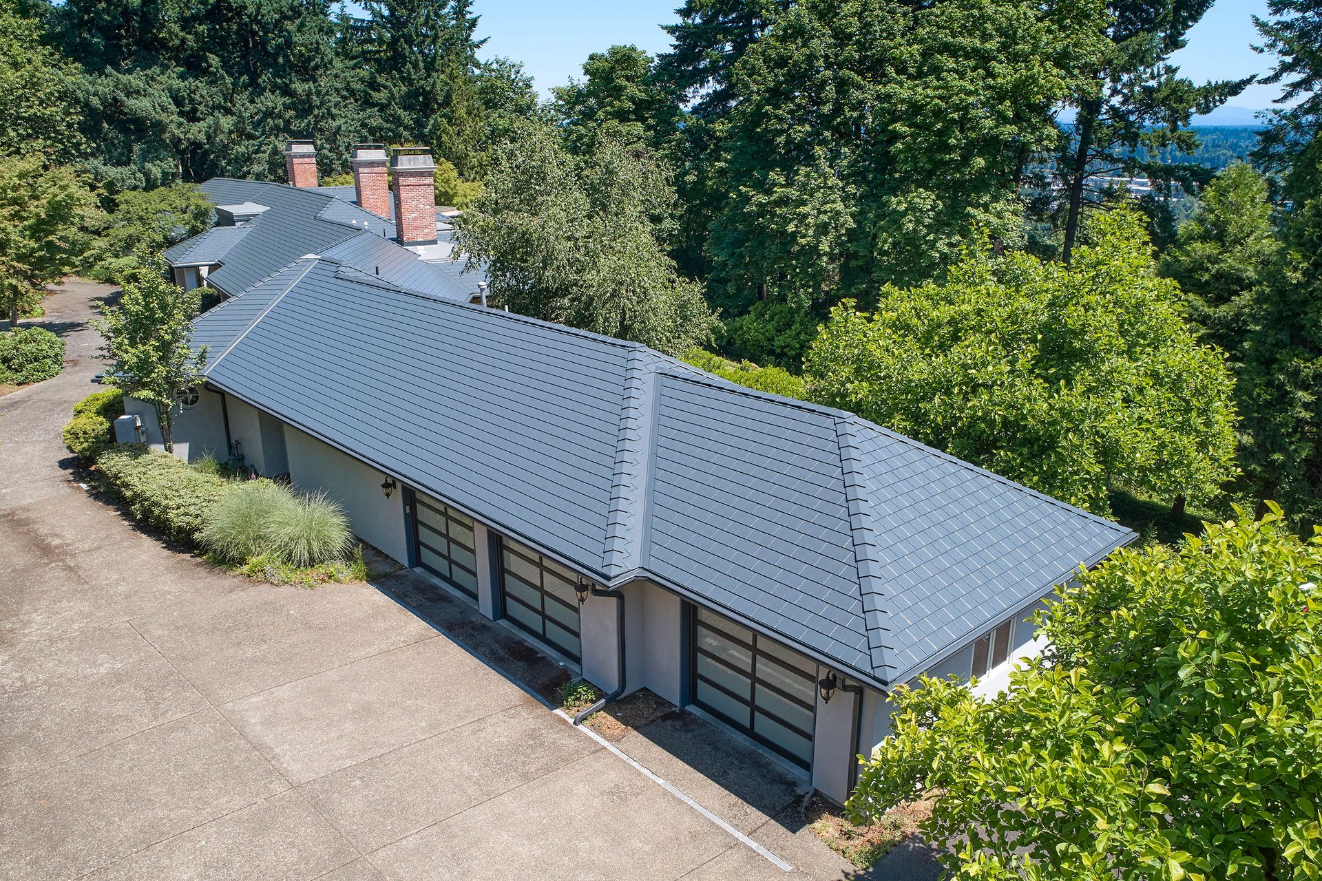 Overhead view of a large home in Dunthorpe, Portland, OR featuring a Deep Charcoal Interlock Slate aluminum roof. The metal roofing system, installed by Interlock Metal Roofing, showcases a clean ridge cap detail and custom flashing around vent pipes, surrounded by mature Northwest landscaping.