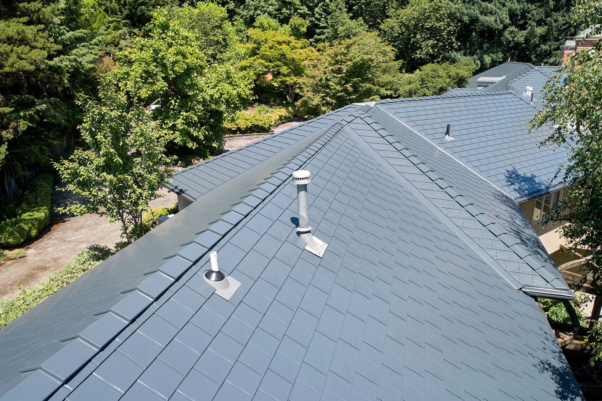 Aerial view of a luxury home in Dunthorpe, Portland OR, featuring a deep charcoal Interlock aluminum slate roof installed by Interlock Metal Roofing. The heavy-gauge metal shingles offer premium durability, fire resistance, and curb appeal surrounded by mature evergreens and landscaping.