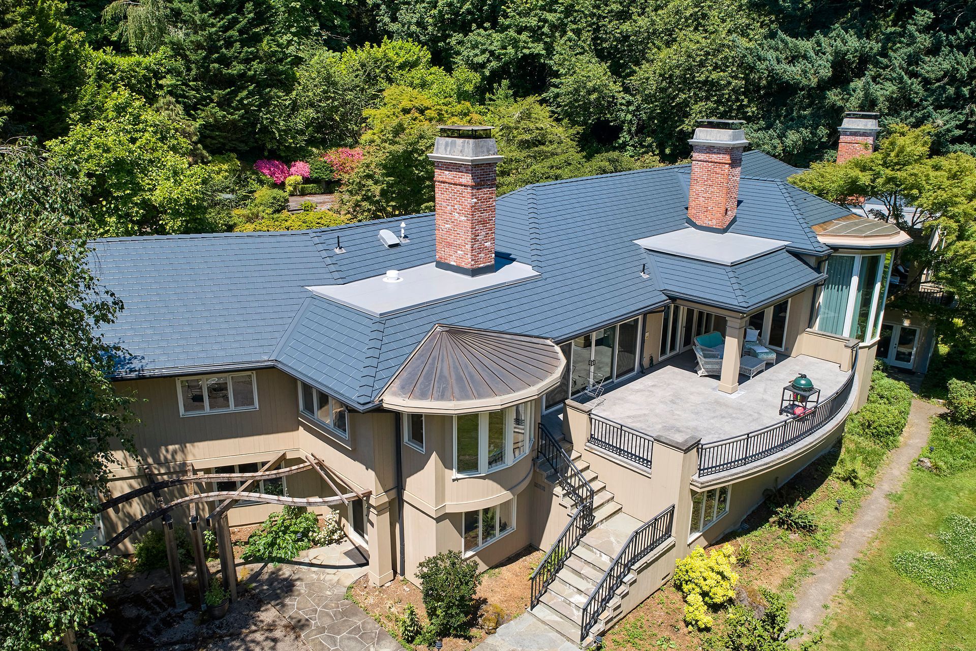 Rear angle showing a luxury two-story Portland OR home in Dunthorpe with a curved architectural balcony and a deep charcoal aluminum slate roof by Interlock Metal Roofing. Combines durability with high-end aesthetics.