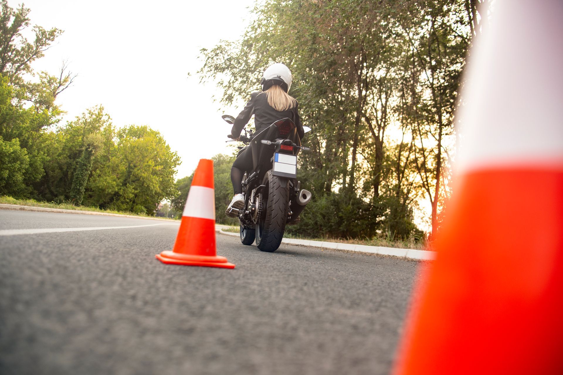 A woman is riding a motorcycle down a road next to a traffic cone.