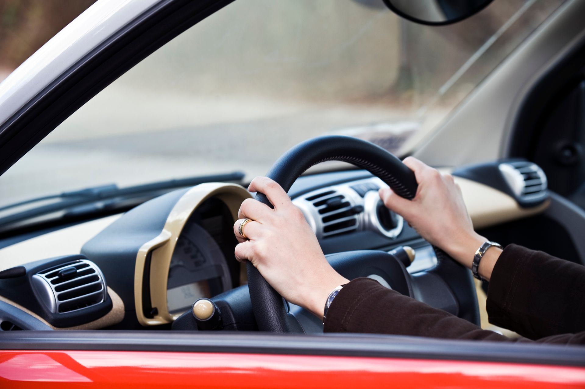 A person is driving a red car with their hands on the steering wheel