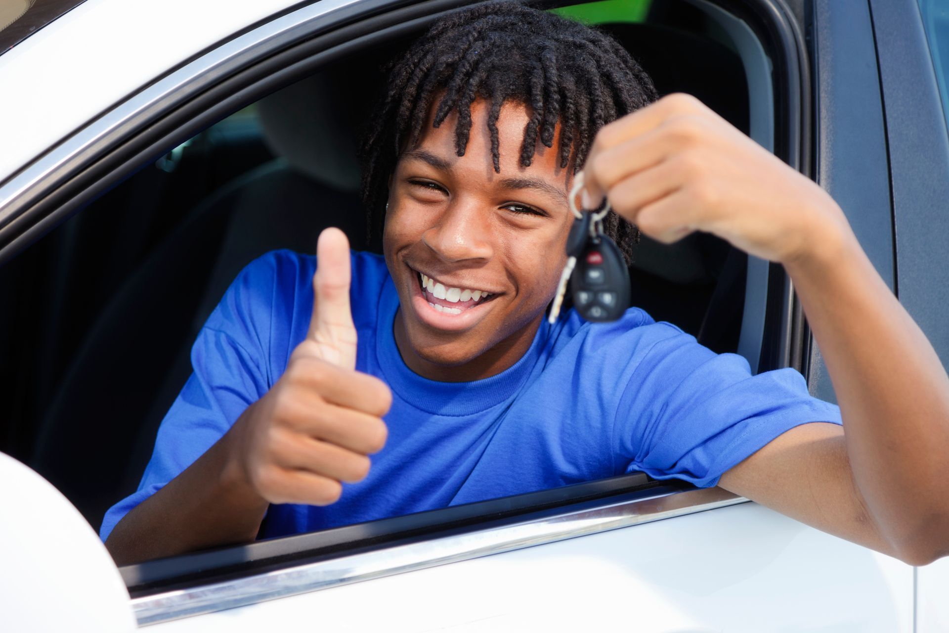 A young man is giving a thumbs up while holding a car key.
