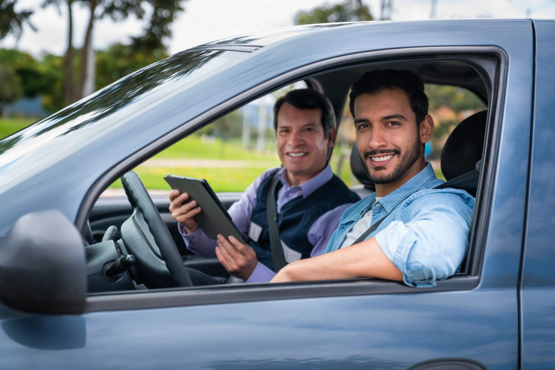 Two men are sitting in a car looking at a tablet.