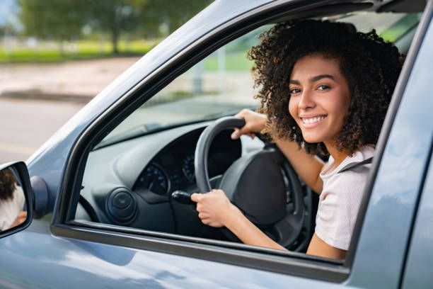 A woman is driving a car and smiling at the camera.
