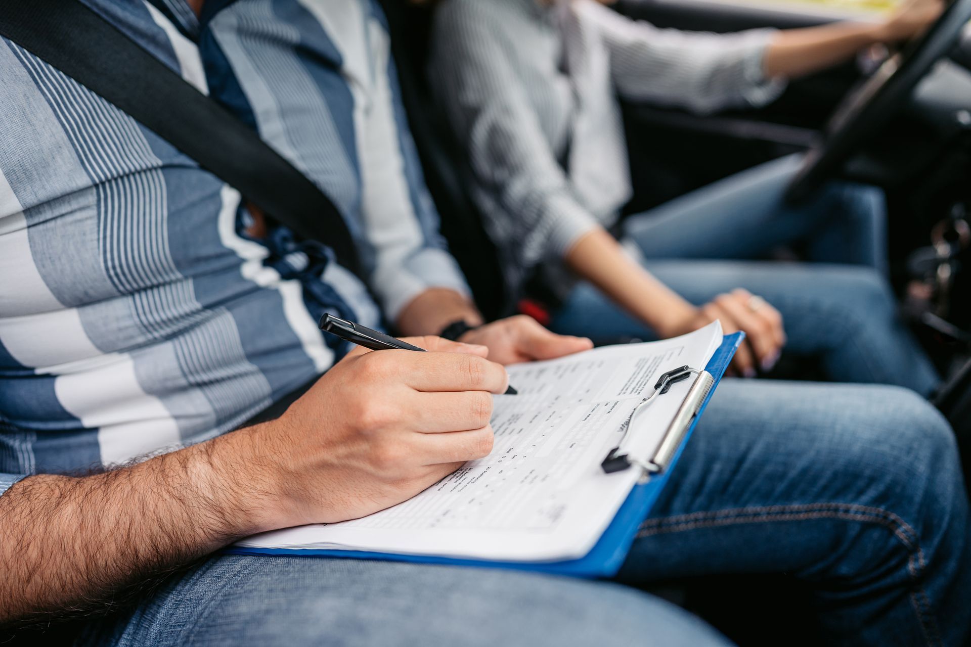 A man is writing on a clipboard while sitting in a car.