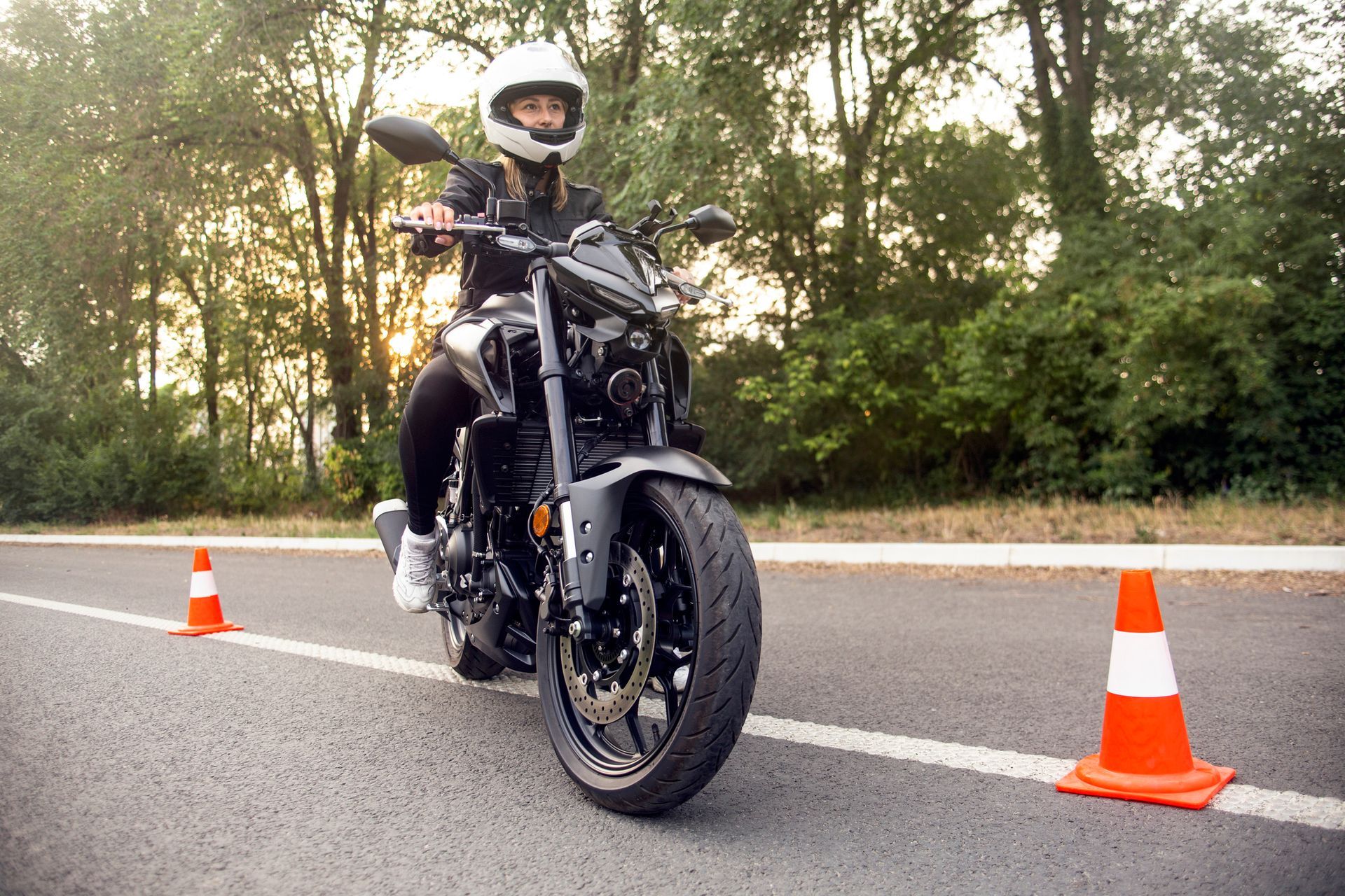 A woman is riding a motorcycle down a road next to traffic cones.