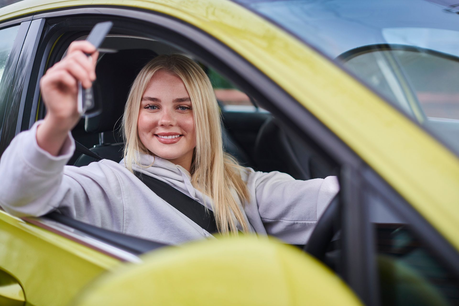 A woman is sitting in a yellow car holding a car key.