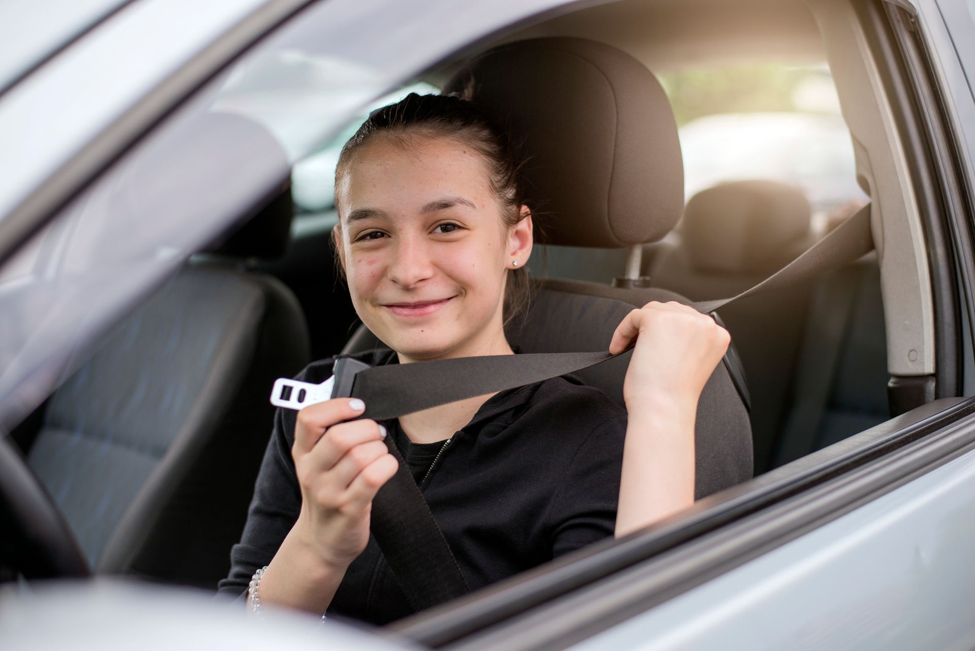 A young girl is putting on her seat belt in a car.