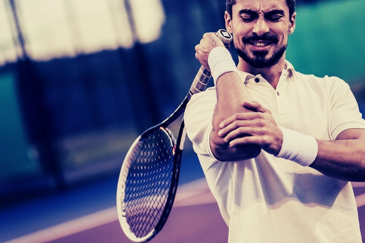 Um homem segura o cotovelo enquanto segura uma raquete de tênis.