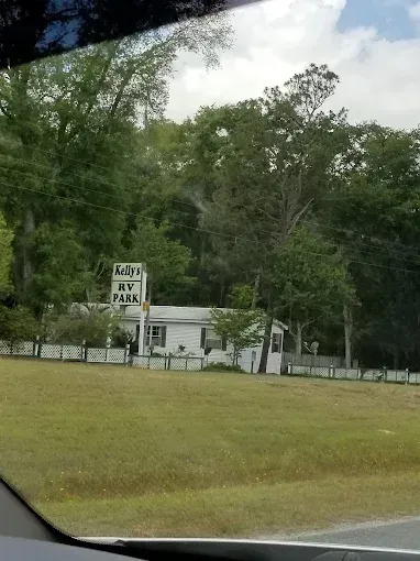 Kelly's RV Park. White building with sign in front of a treeline. Green field in foreground.