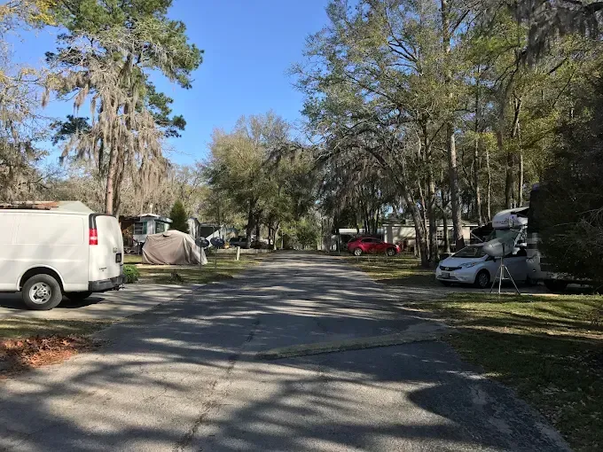 Asphalt road in a campground, lined with RVs, cars, and trees on a sunny day.