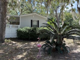 Small, gray house with black shutters, white porch, and pink flamingo yard decoration.