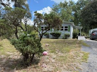 White house with green shutters, small lawn, driveway, car.