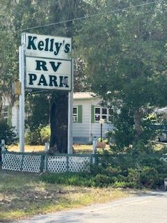 Sign for Kelly's RV Park, with a small white building and green shutters behind it.