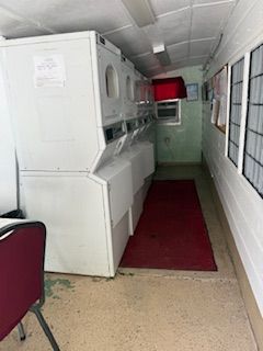 Laundry room with white machines, red rug, and a red chair.