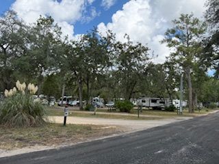Camping area with RVs parked among trees under a cloudy sky.