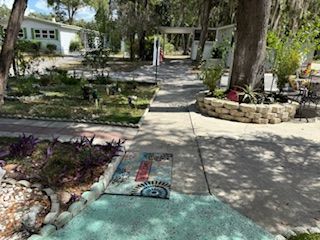 Sidewalk through a garden with a house in the background and colorful mosaics on the path.