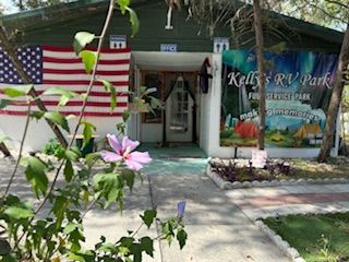 Kelly's RV Park entrance with US flag, flower in foreground, and camping scene sign.