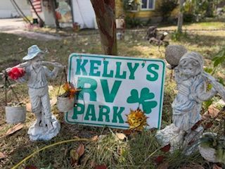 Sign for Kelly's RV Park, with a clover, flanked by statues in a yard.