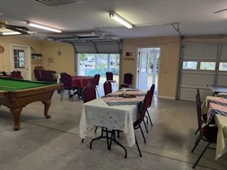 A community center with a pool table, tables, and chairs. Garage door is open.