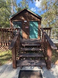 Wooden cabin with steps, teal door, and deck railing in a wooded area.
