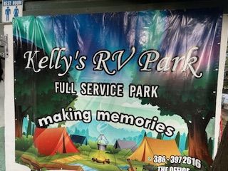 RV campground with trees, asphalt road, RVs parked along the sides.