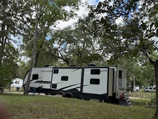 RV parked in a grassy campsite with trees overhead under a cloudy sky.