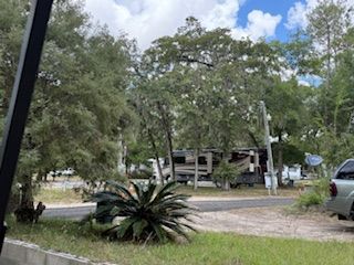 RV parked at campsite amidst trees and greenery under a partly cloudy sky.