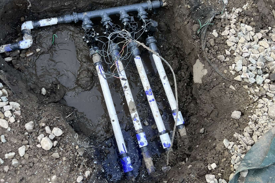 Exposed underground water pipes and valves in a dirt trench with gravel around it