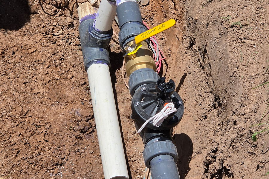 Buried water pipes with black fittings and a yellow valve in a dirt trench