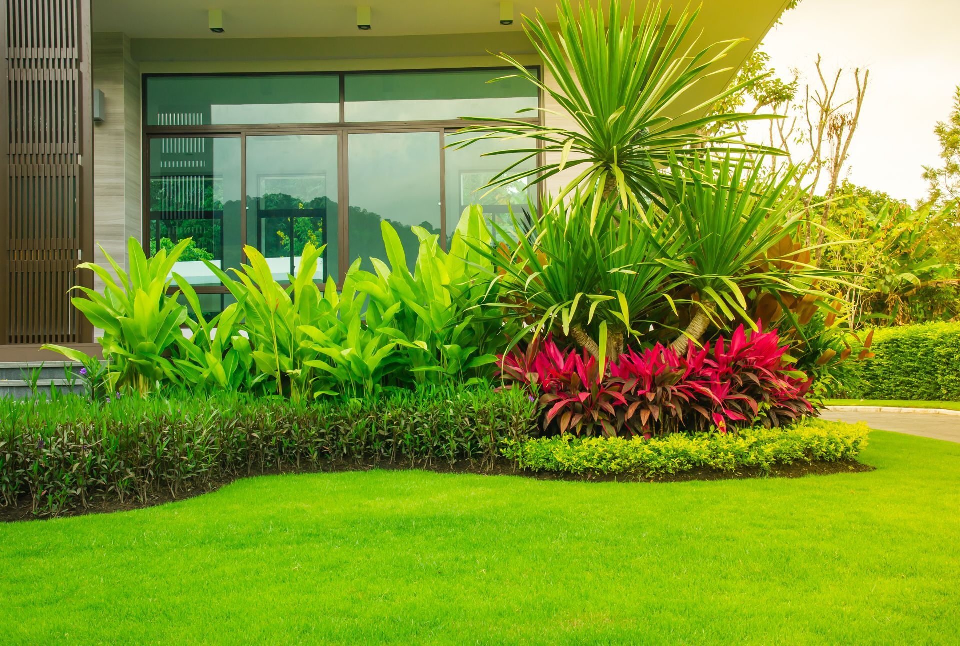 Lush landscaped garden with bright green lawn, tropical plants, and a modern building entrance behind it