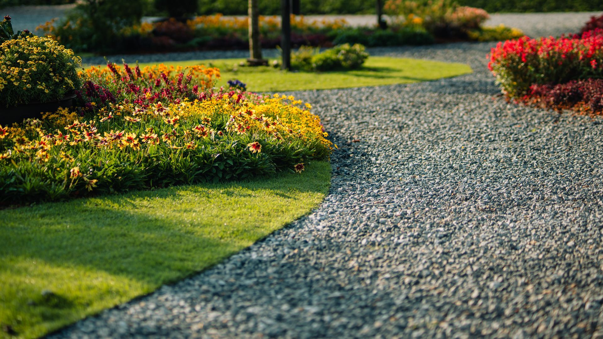Curved gravel garden path beside green lawn and colorful flower beds in sunlight