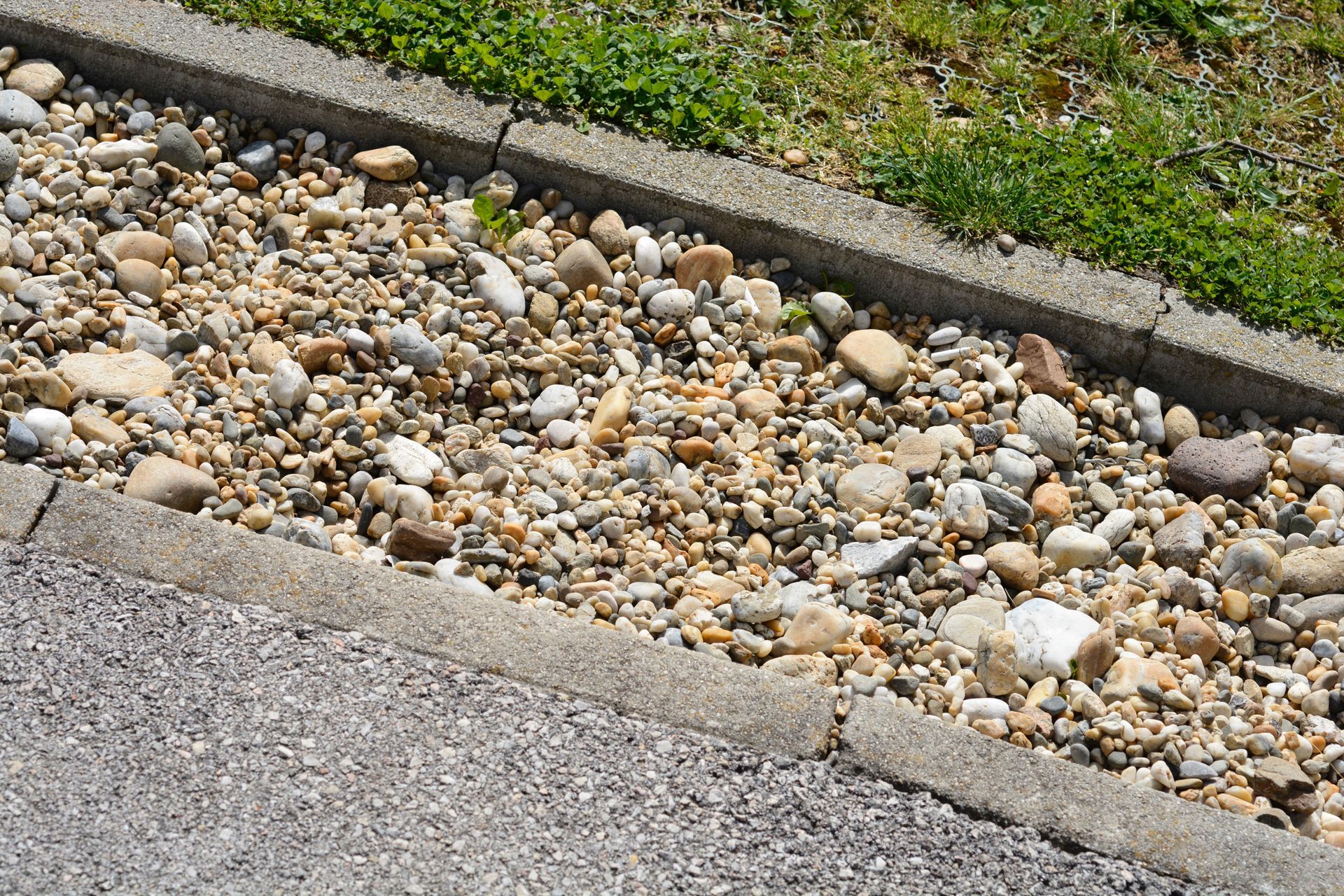 Gravel drainage strip beside concrete curb and sidewalk, with green grass at the top.
