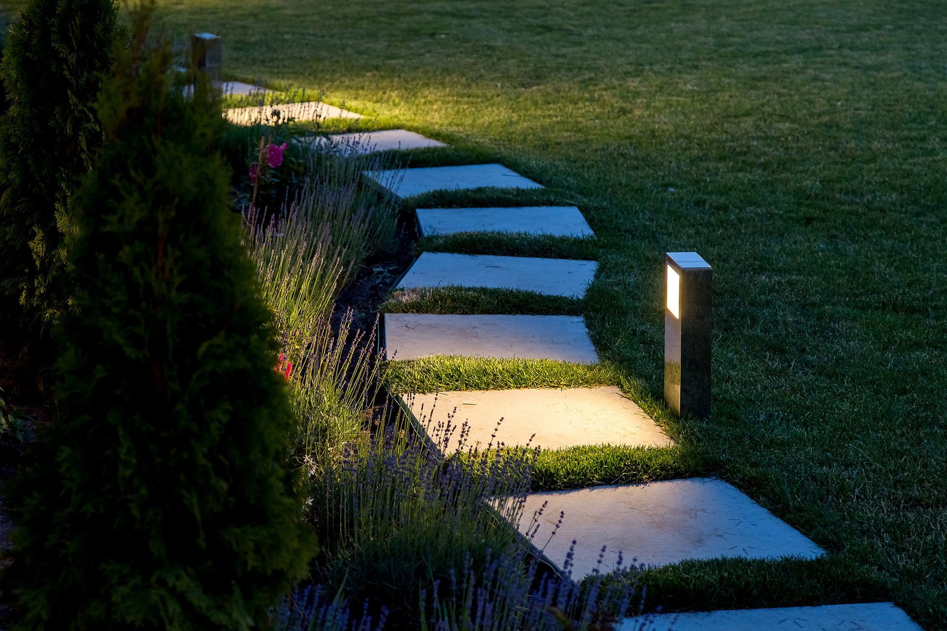Curved garden stepping stones lit by small landscape lights at dusk