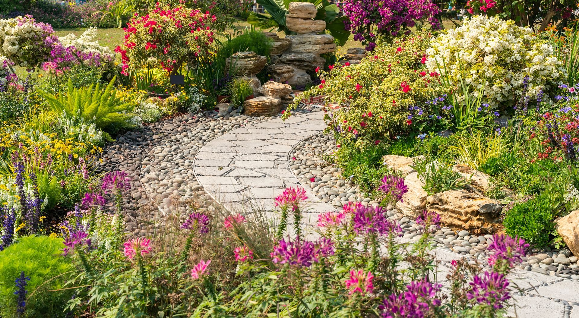 Stone path winding through a colorful flower garden with pink, yellow, and white blooms