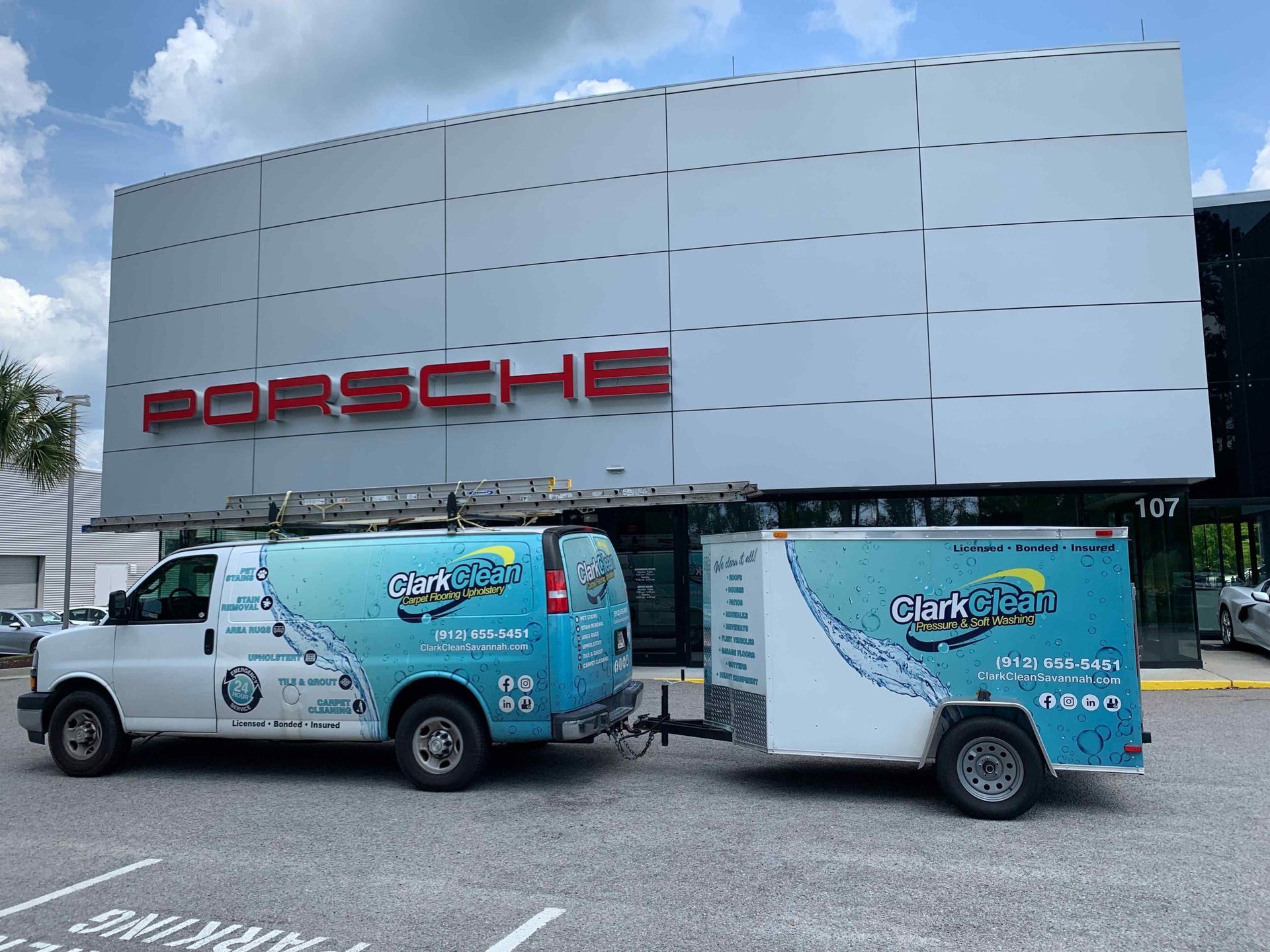 Two vans are parked in front of a porsche building.