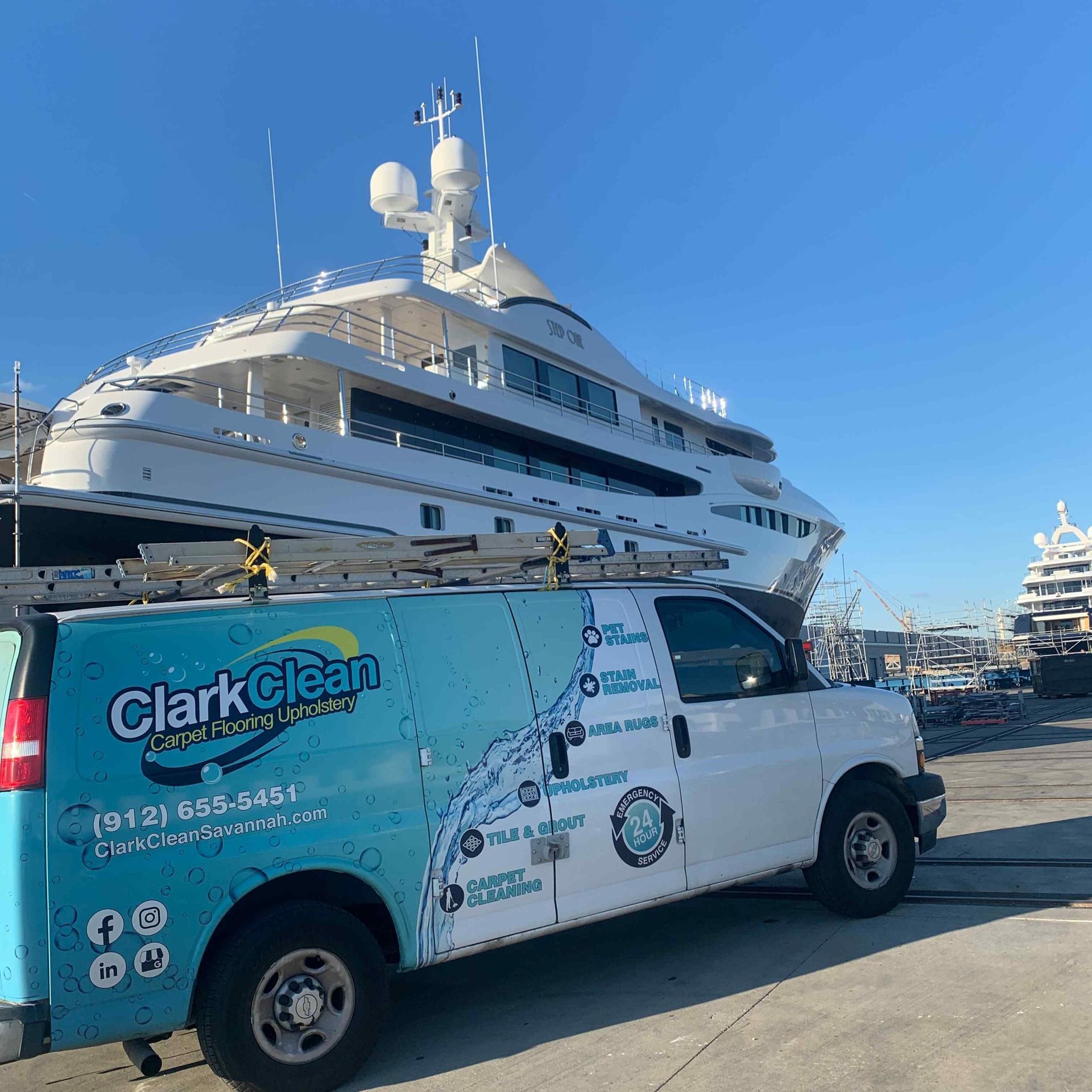 A clark clean van is parked in front of a large boat.