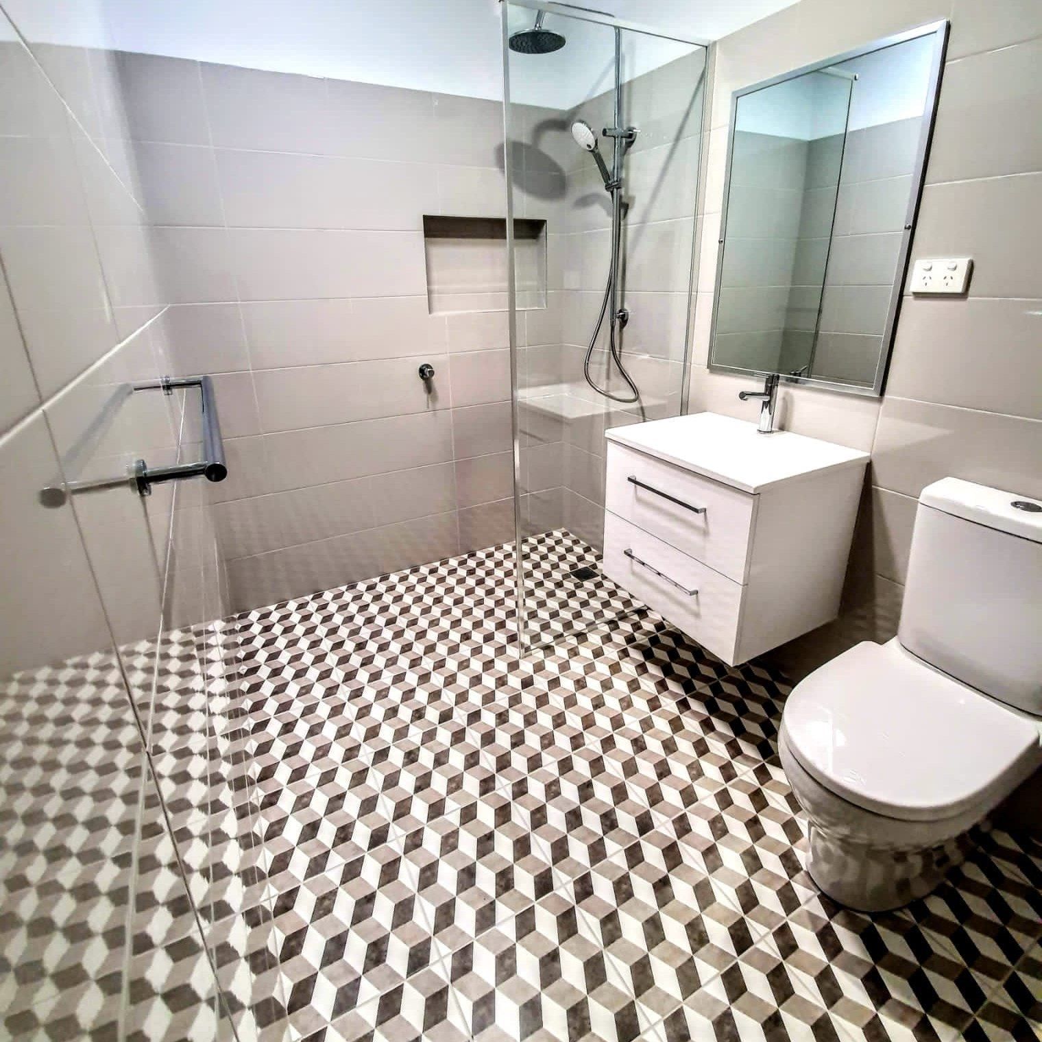 A bathroom with a toilet, sink, shower and mirror.
