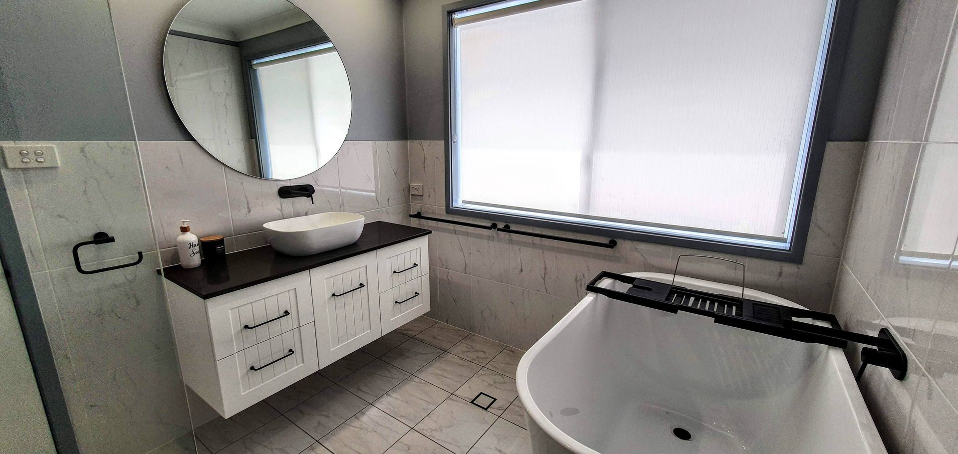 A bathroom with a tub, sink, mirror and window.