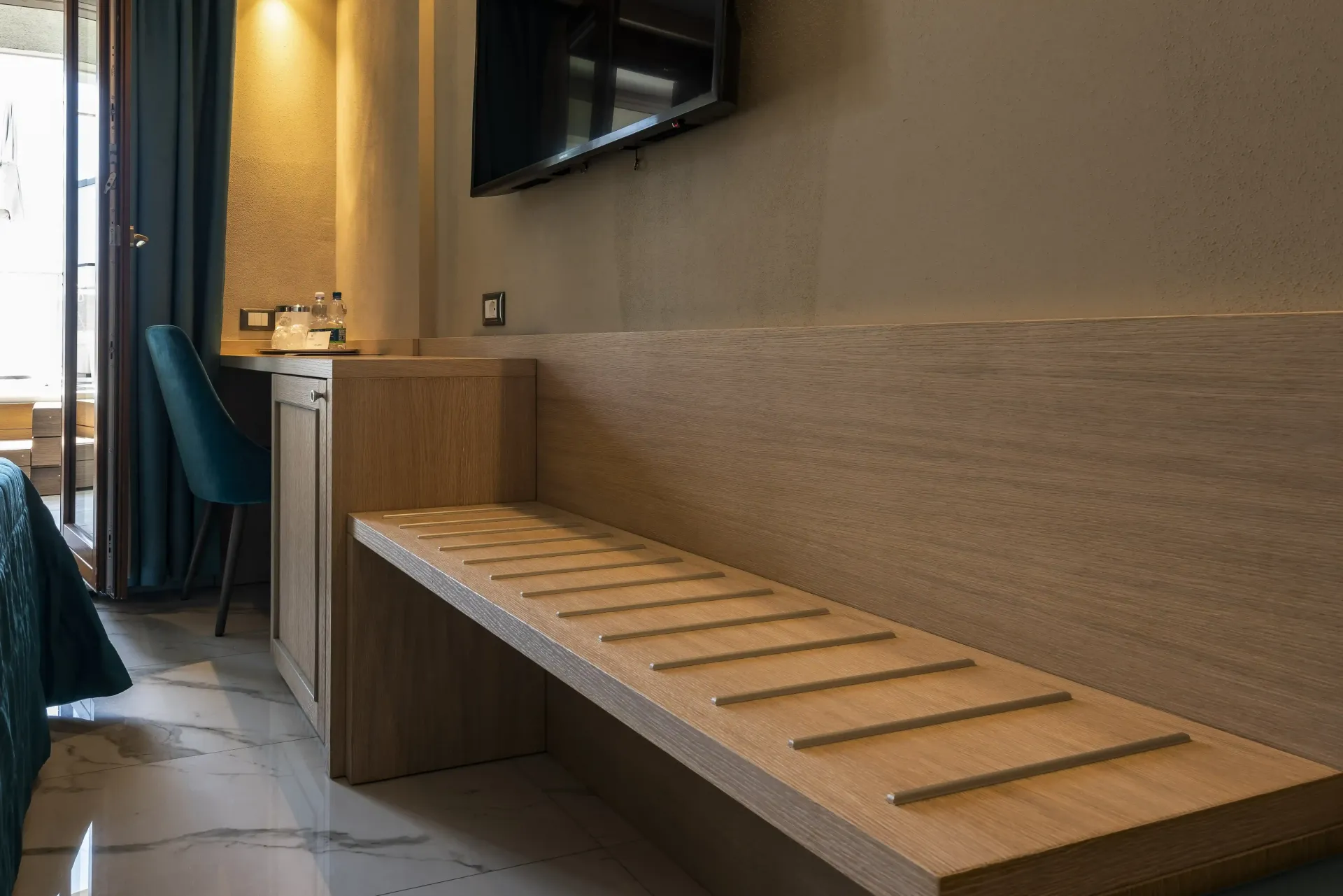 Una stanza d'albergo con una panca e una televisione sul muro