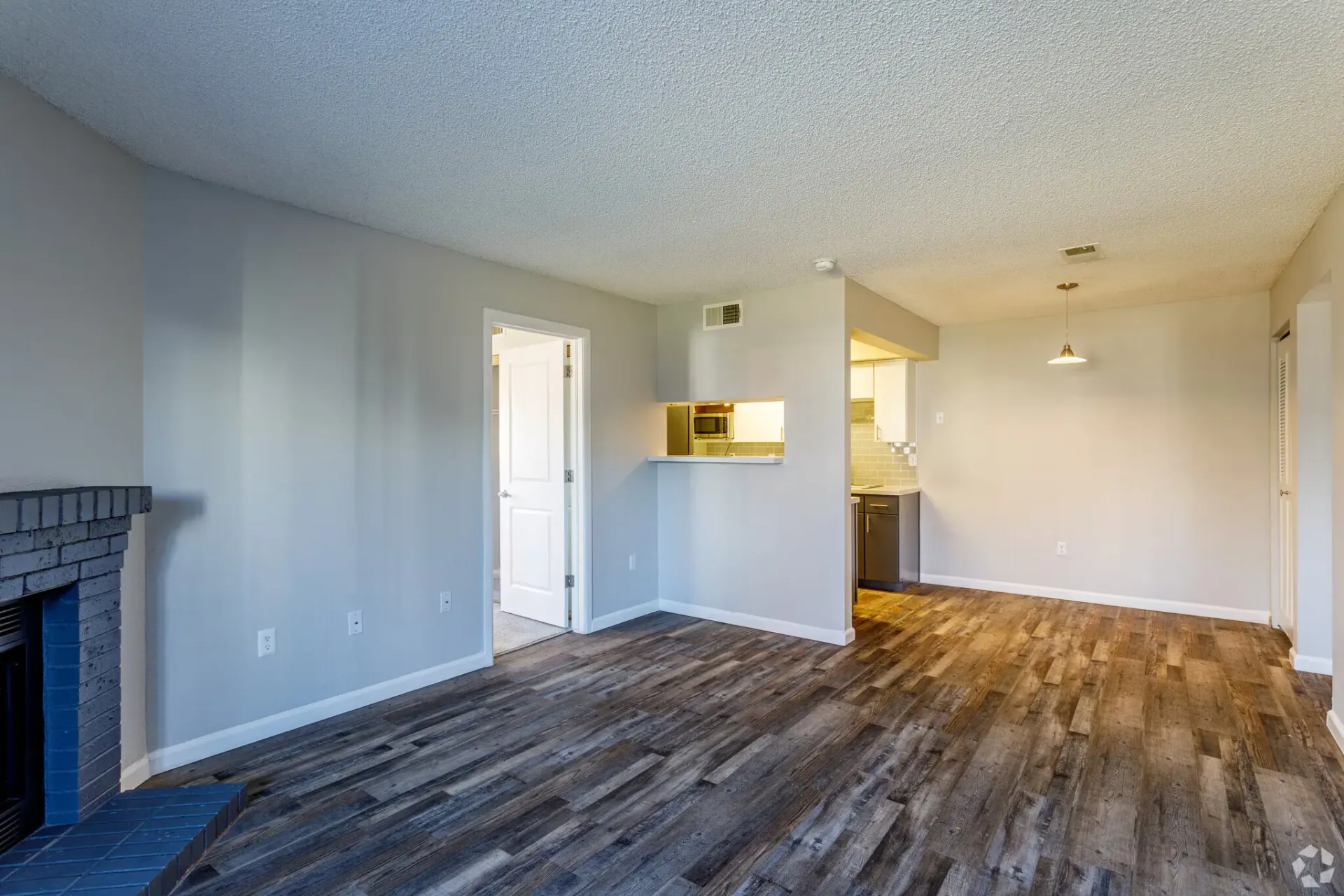 Empty apartment living room with wood-look flooring, fireplace, and open kitchen area at Westward Heights in Denver, CO.