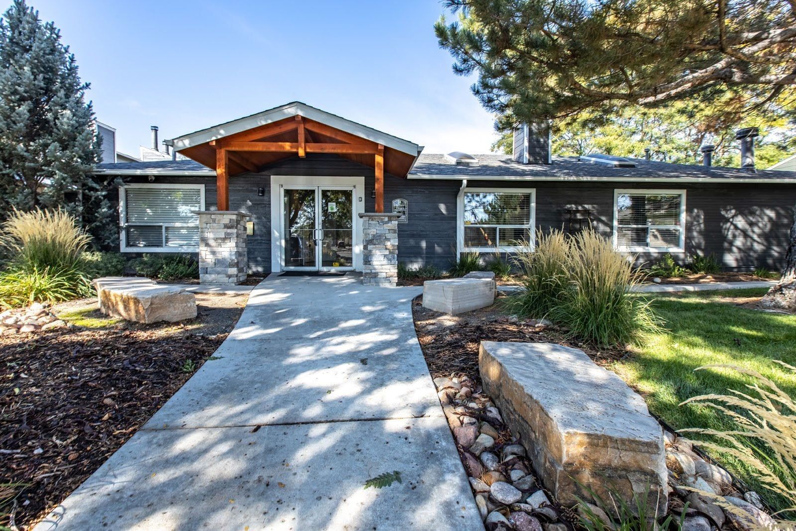 Gray building with a wooden entry, stone accents, and two rock benches in the front yard at Westward Heights in Denver, CO.